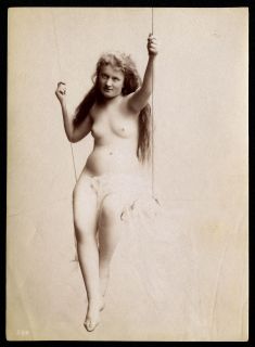 Jeune femme posant assise de face sur une balancoire les seins denudes